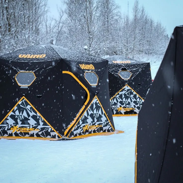 Black and yellow Väinö Extreme XL insulated shelters standing in a snowy forest in daylight